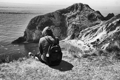 Rear view of person sitting with backpack on sea shore
