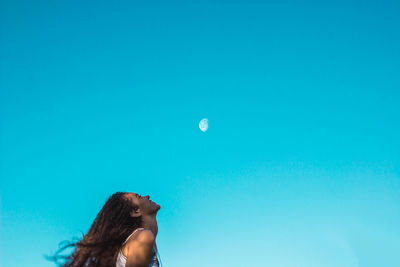 Low angle view of young woman against blue sky