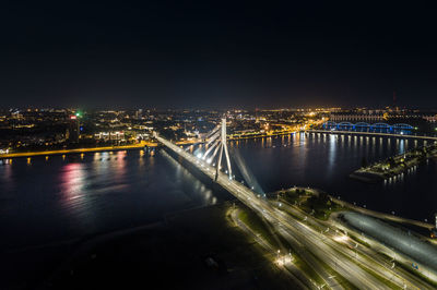 Illuminated bridge over river in city against sky at night