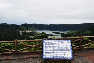 Information sign by fence on mountain against sky