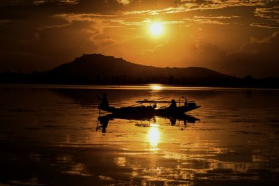 Silhouette man on boat in lake against sky during sunset