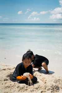 Siblings playing at beach against sky