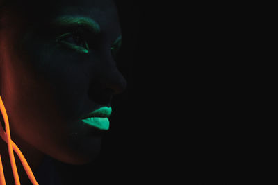 Close-up of woman looking away against black background