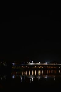 Illuminated buildings by river against sky at night