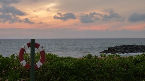 Life belt hanging on wooden post by sea against sky at dusk