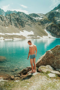 Rear view of shirtless man looking at lake against mountain