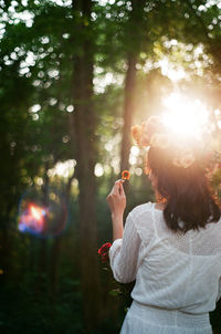 Rear view of woman with flowers standing against trees