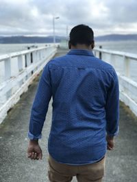 Rear view of man standing on bridge over sea against sky