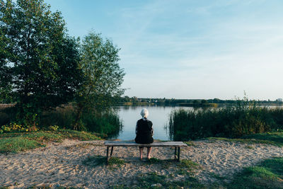 Rear view of man sitting on bench against sky