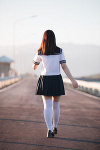 Rear view of woman walking on road against sky