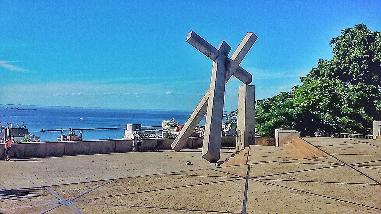 sea, blue, horizon over water, water, sky, clear sky, sunlight, sculpture, day, built structure, nature, beach, tranquility, statue, outdoors, no people, tranquil scene, art and craft, shadow, railing
