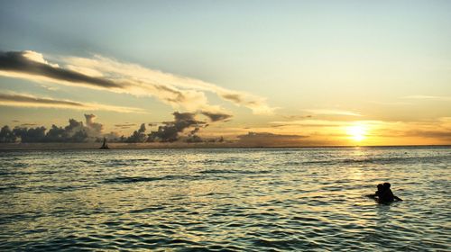 Silhouette swimming in sea against sky during sunset