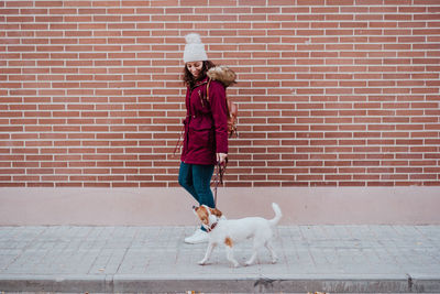 Woman with dog walking on footpath against wall