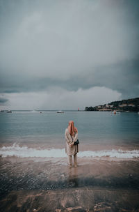 Rear view of woman standing on beach against sky