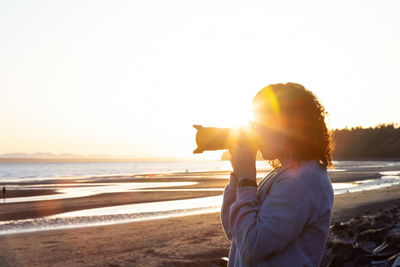 Woman at beach against sky during sunset