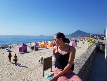 Woman on beach by sea against clear blue sky