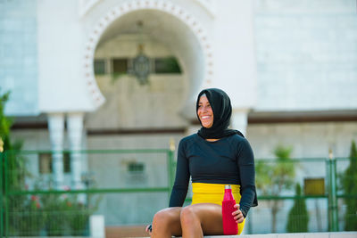 Smiling woman in hijab looking away while sitting outdoors