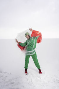 Woman in green bird costume wrapped in plastic against sky