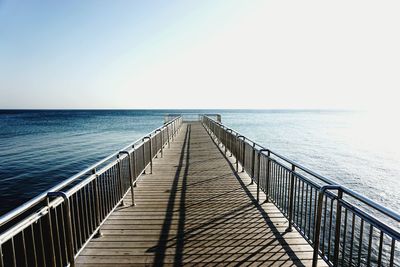 Empty pier at sea against clear sky on sunny day