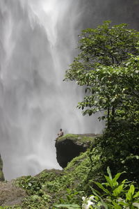 Person sitting on rock by waterfall