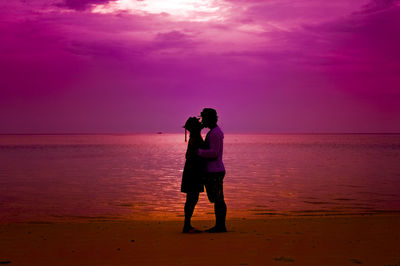 Full length of friends standing on beach against sky during sunset