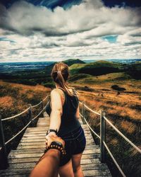 Rear view of woman lying on railing against sky