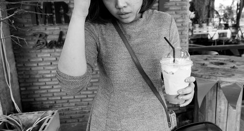 Midsection of woman holding coffee against brick wall