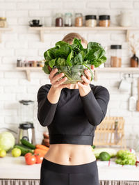 Young woman holding spinach in bowl while standing at kitchen