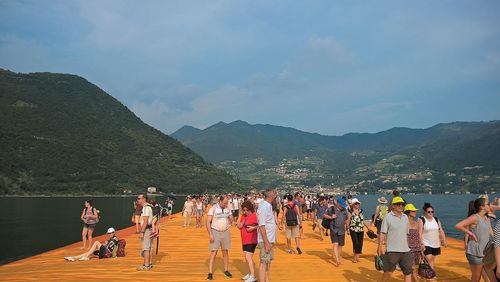 People on wooden pier over lake against sky