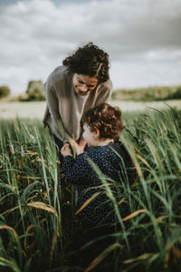 Mother with daughter standing amidst plants against sky