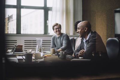 Happy mature businessman sitting by colleagues at conference table in office