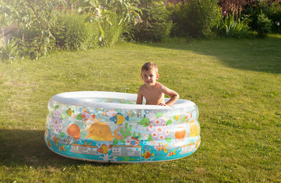 Little boy splashes in an inflatable pool. squints from the spray. backyard vacations concept