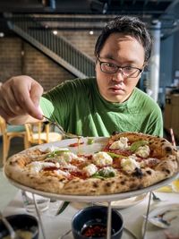 Close-up of asian man holding spoon and dripping chili oil onto pizza bufalina on plate on table.