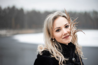 Portrait of smiling beautiful woman holding plant while standing at beach