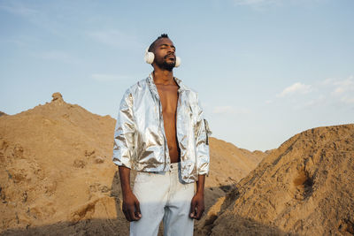 Man with eyes closed listening music through wireless headphones while standing on sand