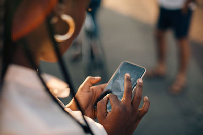 Cropped image of young woman using smart phone while standing on street in city