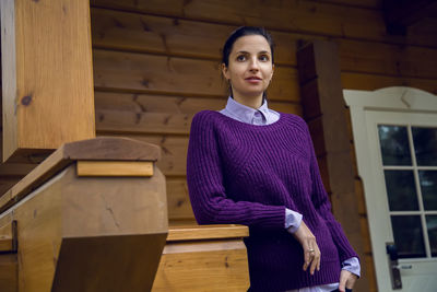 Young woman in a purple sweater and black jeans out on the porch of a wooden house