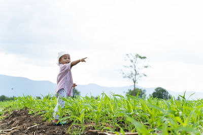 Portrait of boy pointing while standing on field against sky