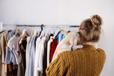 Rear view of woman looking at clothes on rack while holding dog
