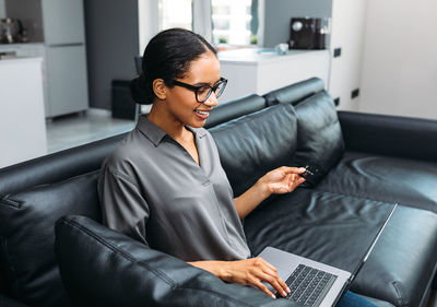Smiling woman using laptop while sitting on sofa