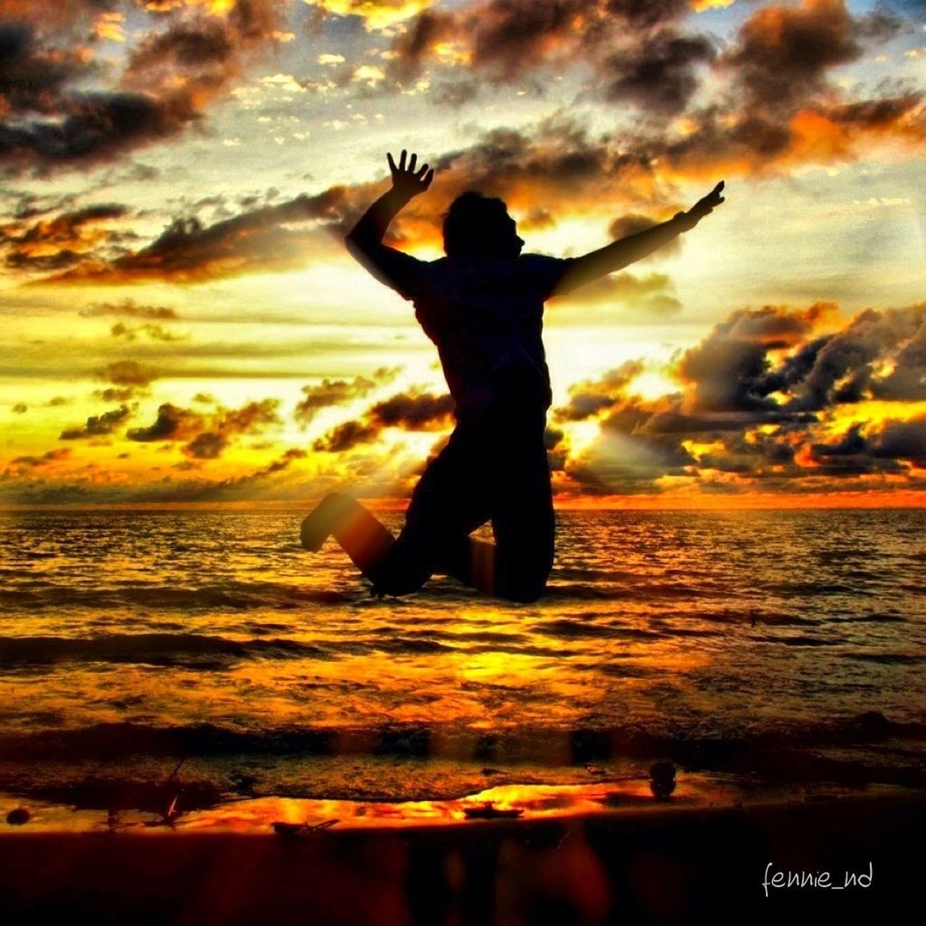 sunset, sky, lifestyles, leisure activity, sea, silhouette, cloud - sky, beach, orange color, full length, water, standing, dramatic sky, arms raised, scenics, person, horizon over water, beauty in nature