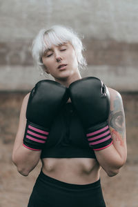 Woman with boxing gloves standing against wall