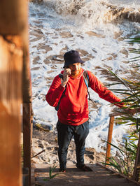 Bearded millennial man in red hoody backpack autumn sea dry reed authentic hipster tourist lifestyle