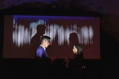 Side view of business colleagues discussing by projection screen in illuminated workshop