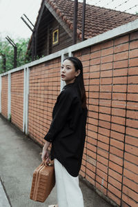 Young woman looking away while standing against building