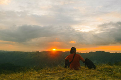 Rear view of woman sitting on field against sky during sunset