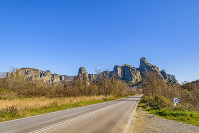 Road amidst trees against clear blue sky