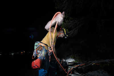 Man coiling rope after climbing during the night in the dark headlamp