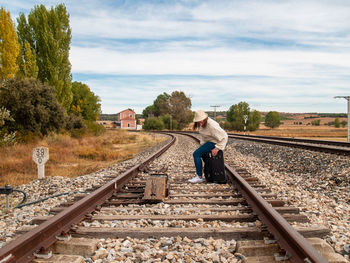 Full length of woman sitting on luggage at railroad track