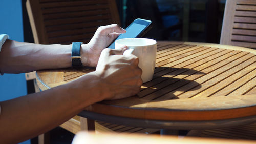 Closeup of asian male hands playing smartphone and drinking coffee